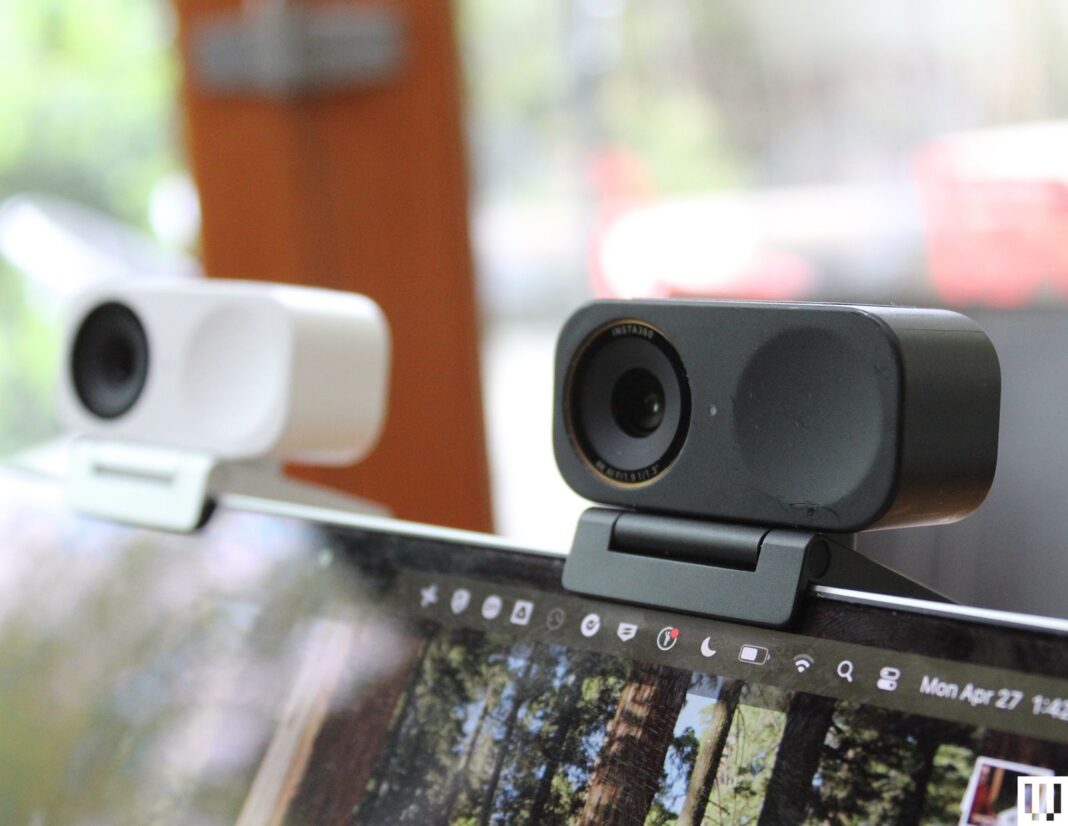 Two small rectangular webcams clipped to the top of a laptop screen one in white and the other black