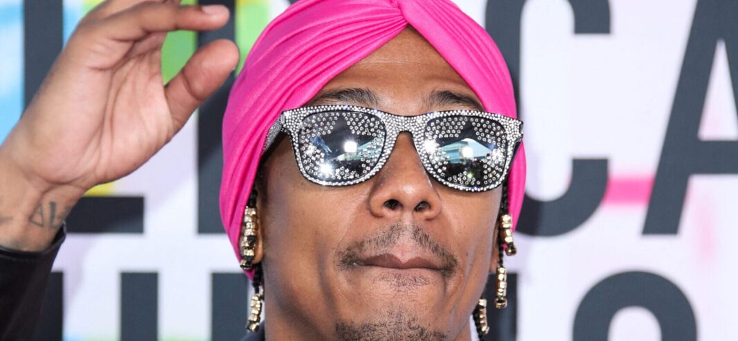 Nick Cannon posing on the red carpet with glasses and a pink turban.